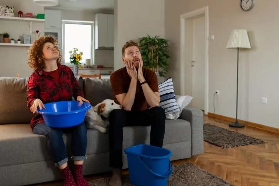 A couple holding BUckets to collect water leak dripping from the ceiling
